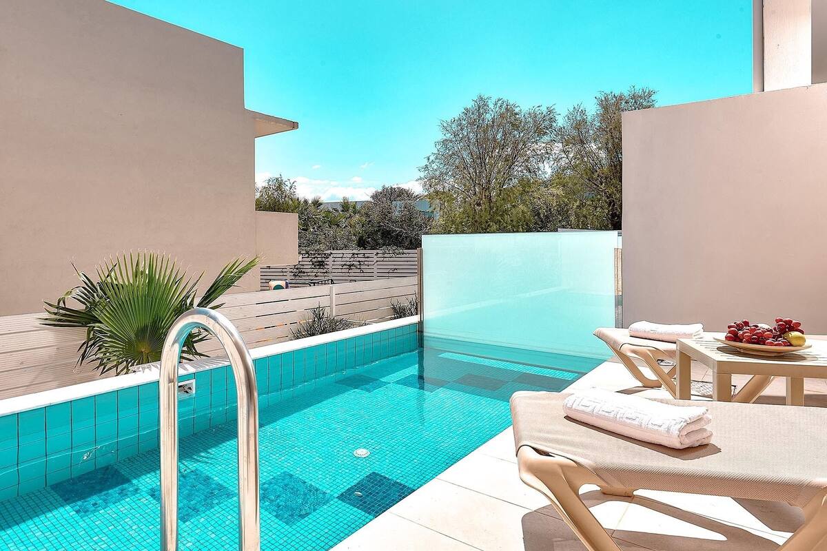 A swimming pool with a clear blue water, surrounded by a wooden deck and a white wall.