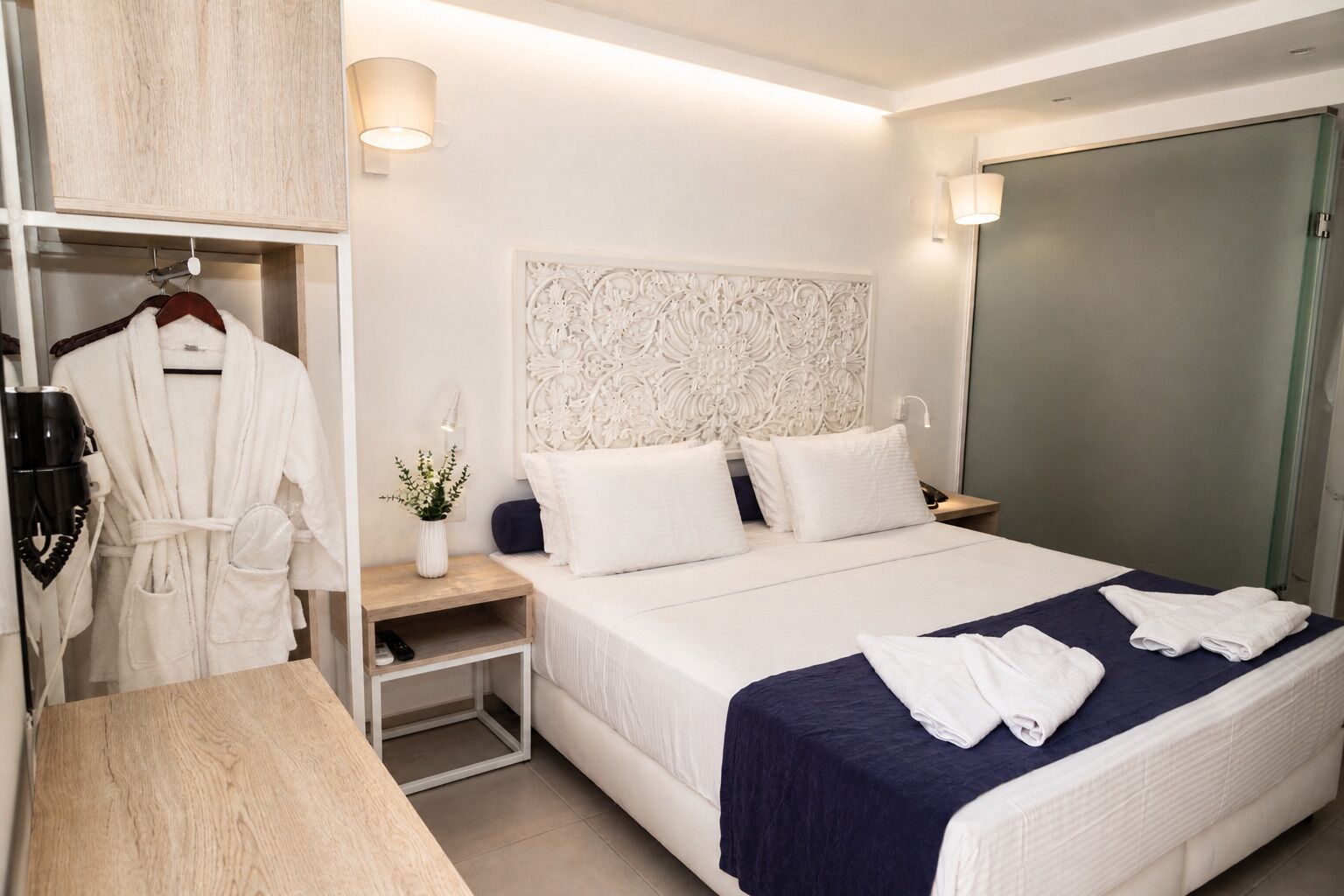 Habitación de hotel con cama, mesita de noche, bata y lámpara fijada a la pared.