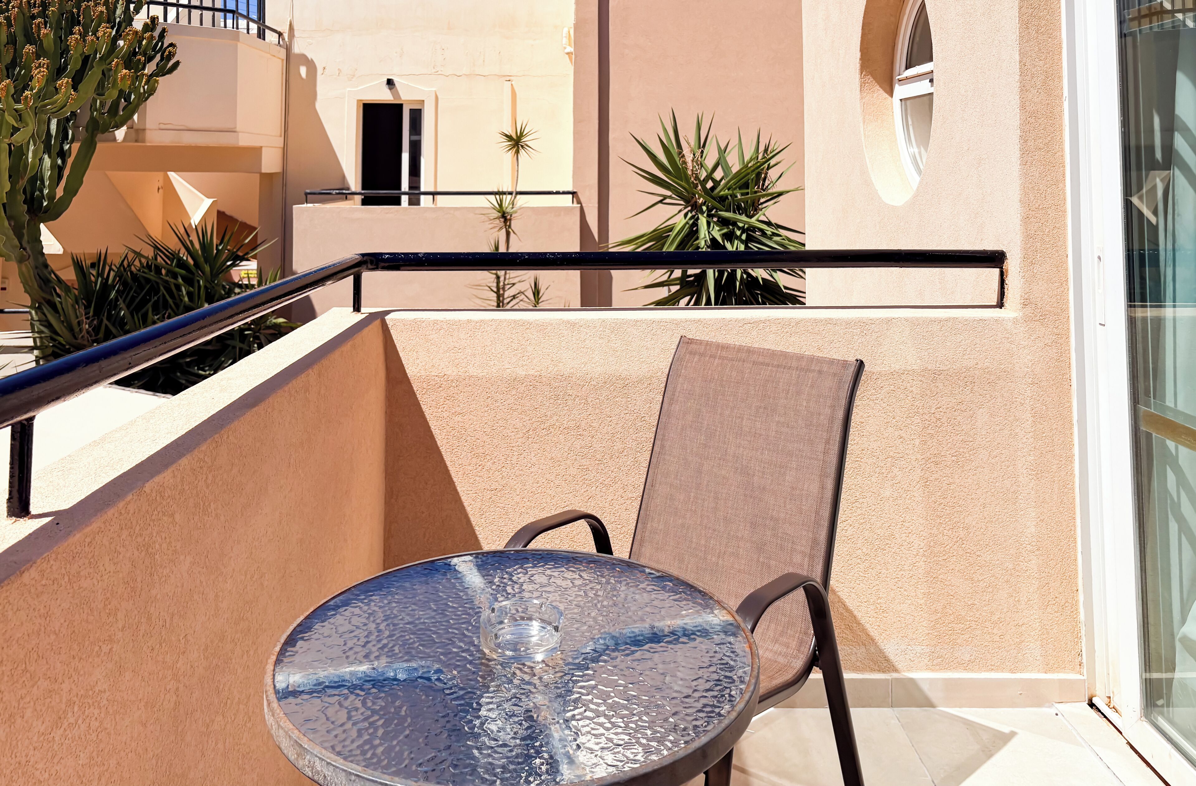 A balcony with a glass table, metal chairs, and potted plants.