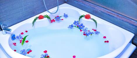 A bathtub with water, flowers, and a shower head.