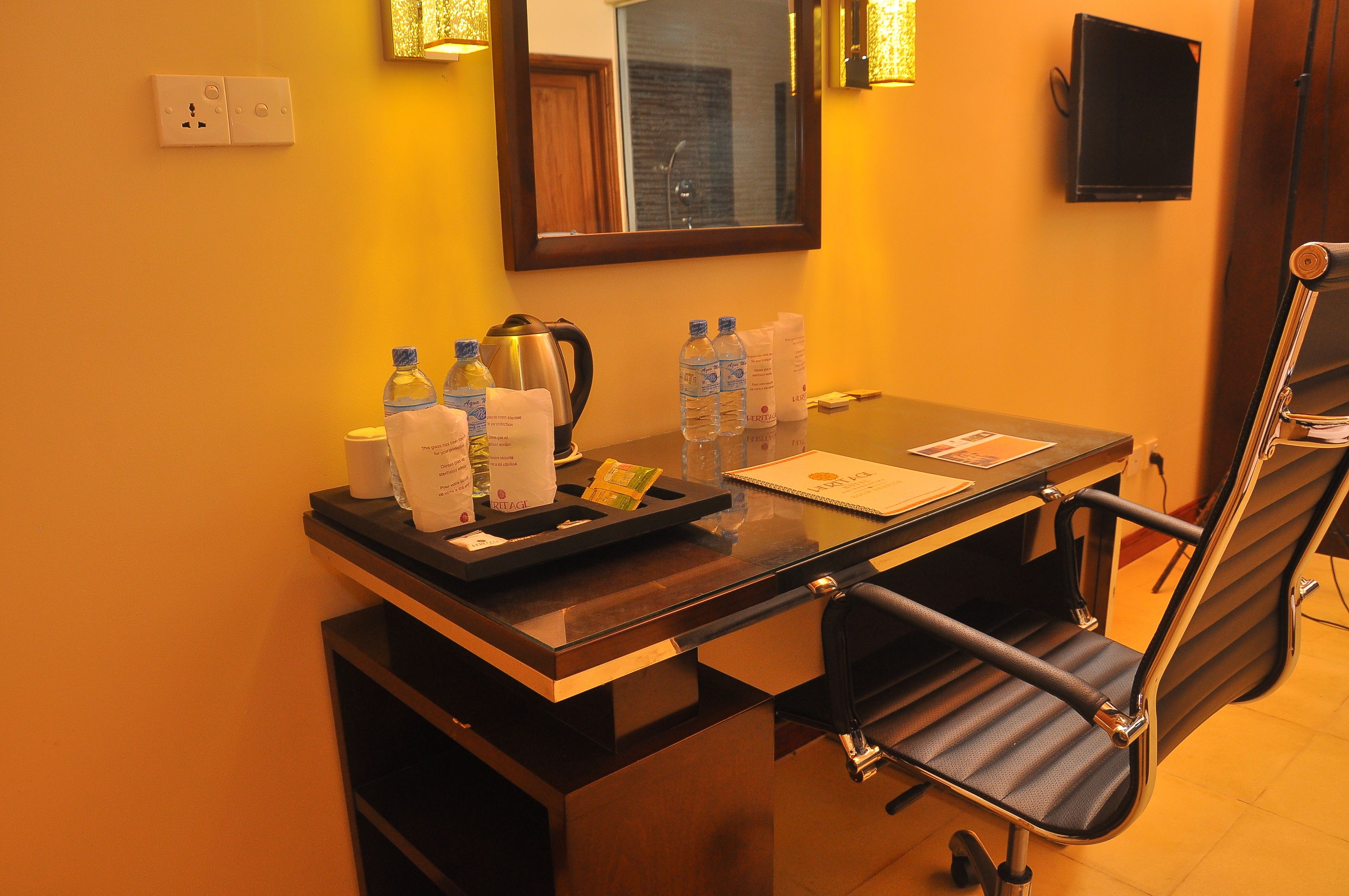 A hotel reception desk with a mirror, a kettle, bottled water, and a notepad.