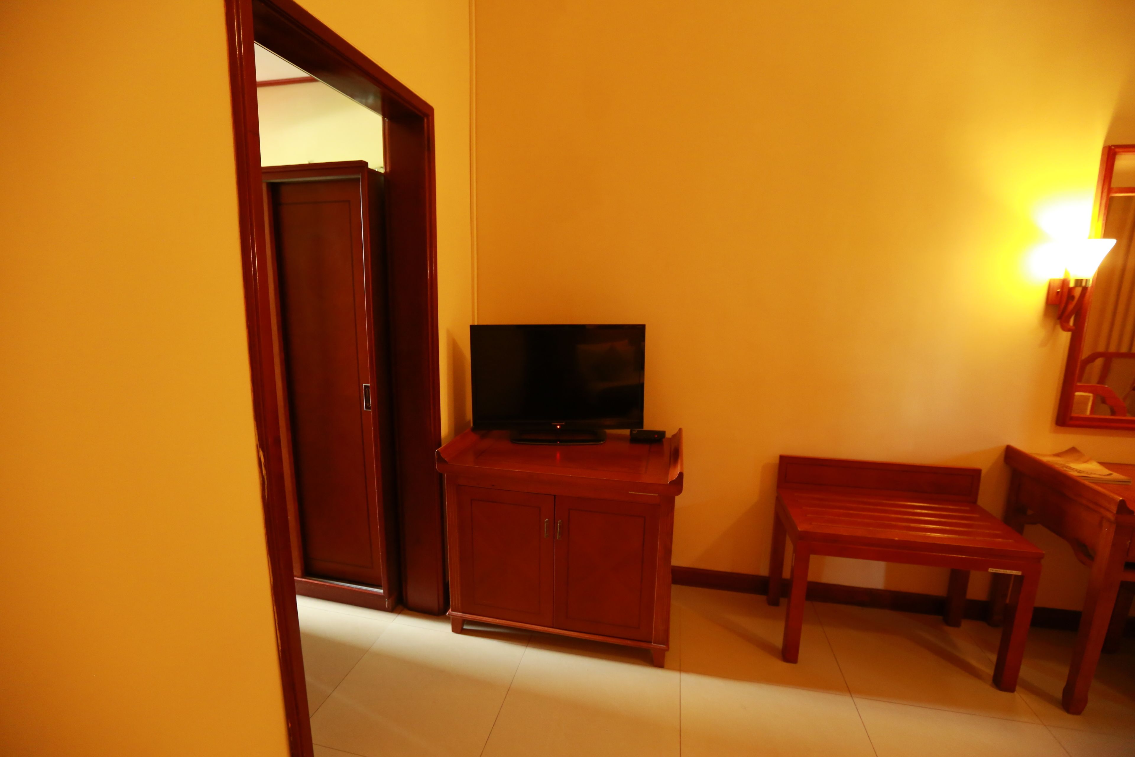 Una habitación con un armario de madera, un televisor, un banco y una puerta.