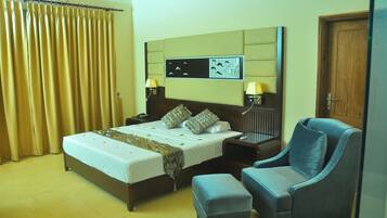 A hotel room with a bed, two bedside tables with lamps, a chair, an ottoman, and a wall-mounted artwork.
