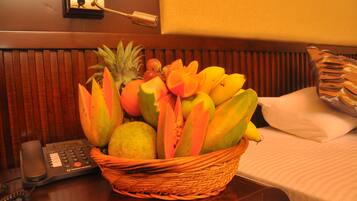 A fruit basket on a hotel room table with a telephone and a wall clock.