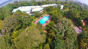 An aerial view of a resort with a swimming pool surrounded by lush greenery, overlooking a large body of water. - Heritage Hotel (Anuradhapura)