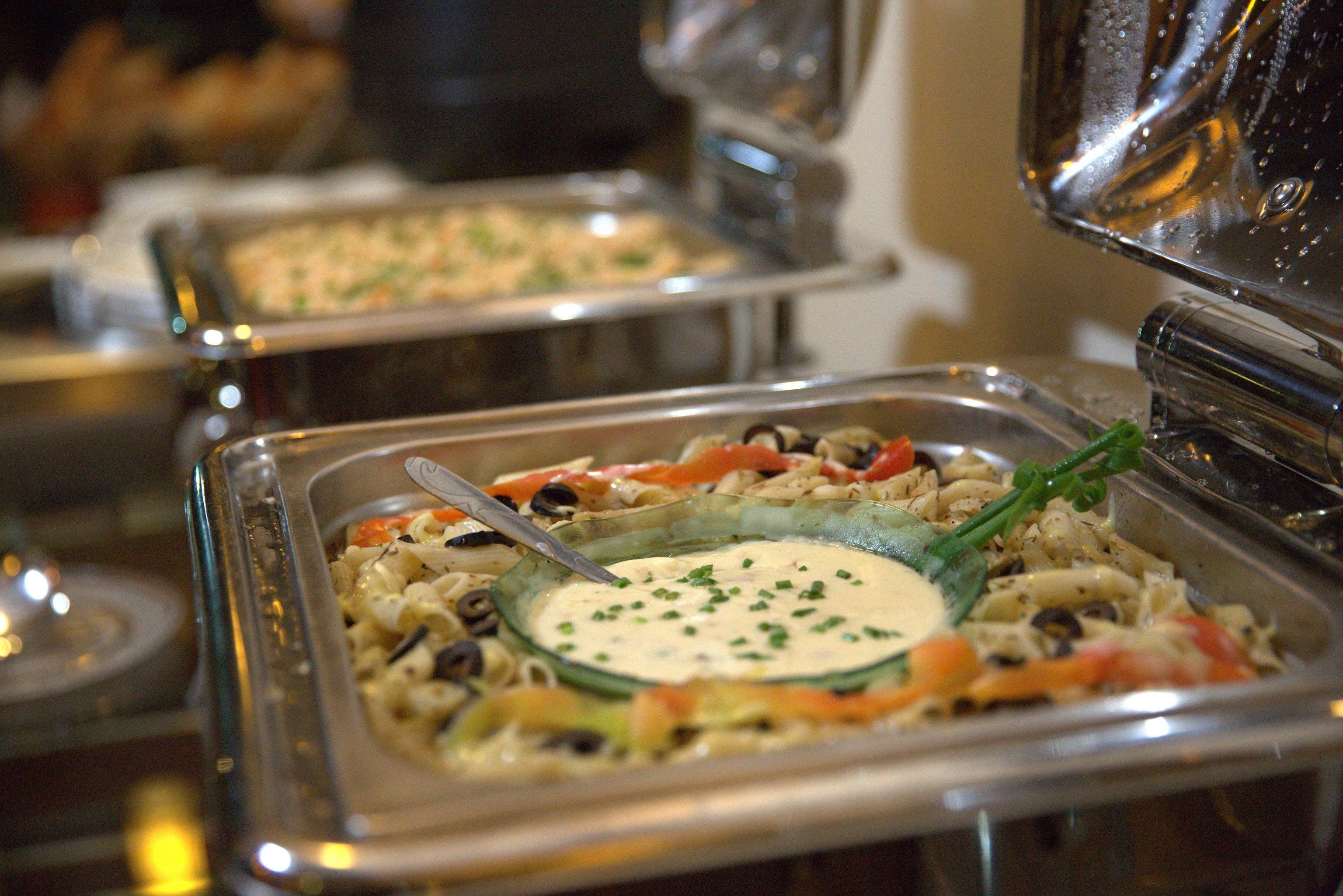 Ein Buffet mit verschiedenen Speisen, darunter Pasta, Gemüse und eine cremige Soße in einer Glasbowl.