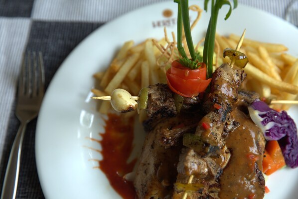 A plate of food with meat skewers, fries, and vegetables. - Heritage Hotel (Anuradhapura)