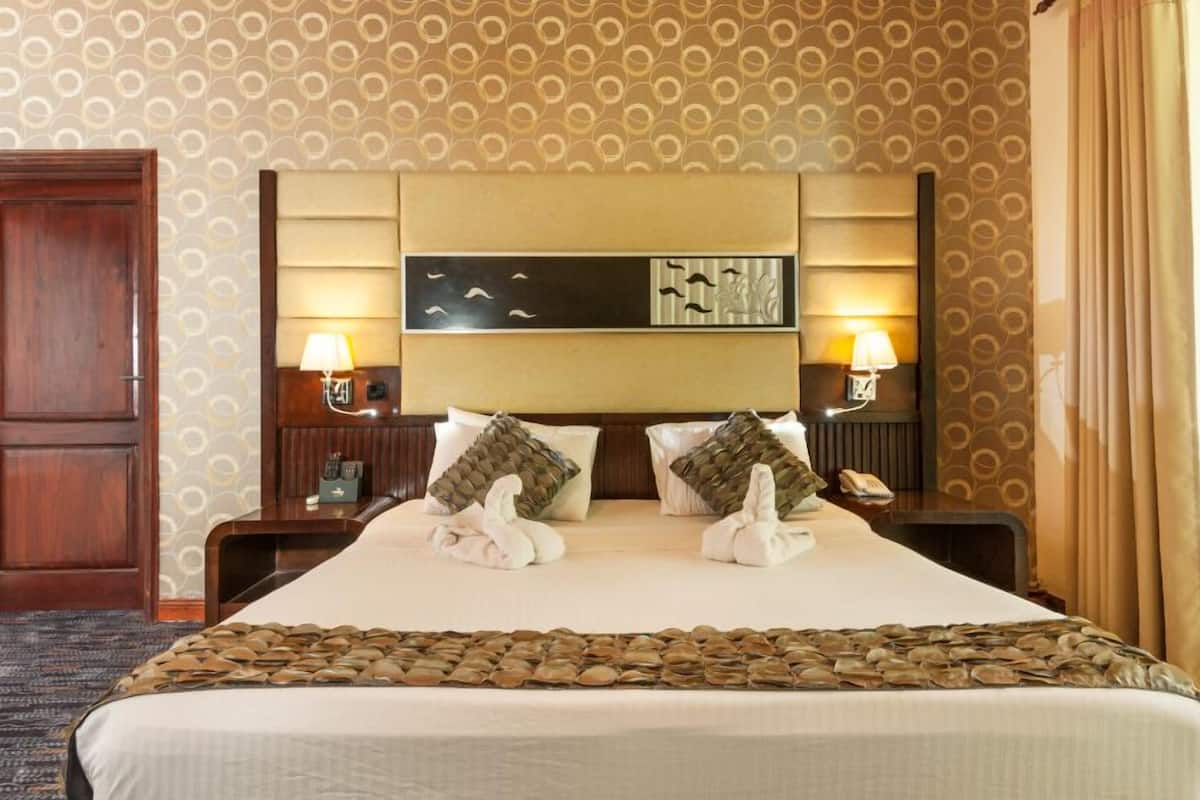 A hotel room with a large bed, two bedside tables, lamps, and a headboard with a decorative panel.