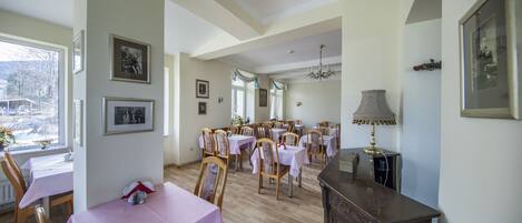 A dining area with multiple tables and chairs, a chandelier, and framed pictures on the walls.