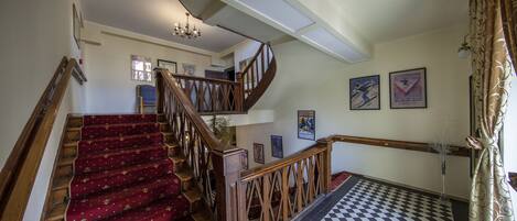 A staircase with red carpeted steps and wooden railings, leading to an upper floor.