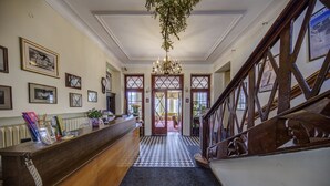 Un espace d’accueil avec un comptoir d’enregistrement, des tableaux encadrés au mur, un lustre et un escalier avec des rampes en bois.