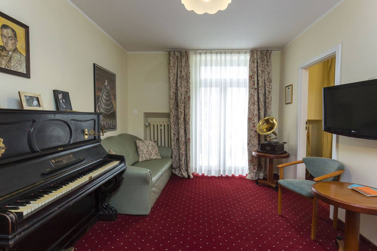 Una sala de estar con un piano, un sofá, un televisor y un tocadiscos.