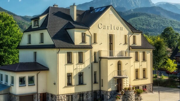 Une maison à deux étages, nommée « Carlton », avec des fondations en pierre, de nombreuses fenêtres et un balcon.