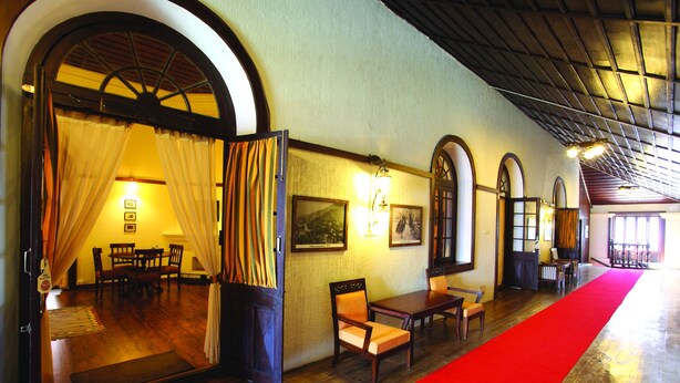 Vestíbulo de hotel con piso de madera, alfombra roja y un área de comedor con mesas y sillas.