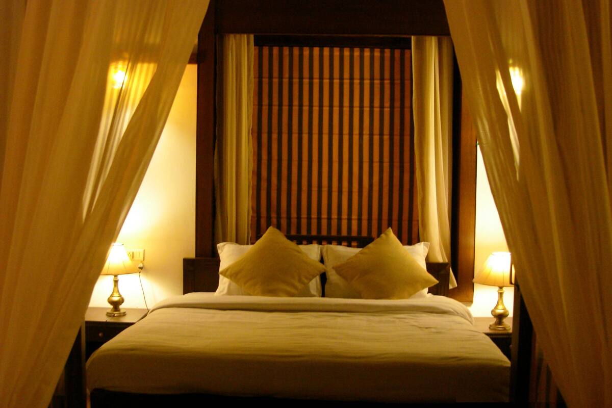 A bed with white linens and two pillows, flanked by two bedside lamps.