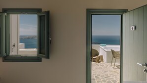 Une porte ouverte donnant sur un balcon doté d’un sol en pierre et offrant une vue sur la mer.