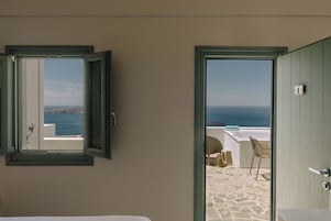 An open door leading to a balcony with a stone floor and a view of the sea.