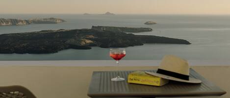 A table with a hat and a glass of red wine, overlooking a coastal landscape with cliffs and calm sea.