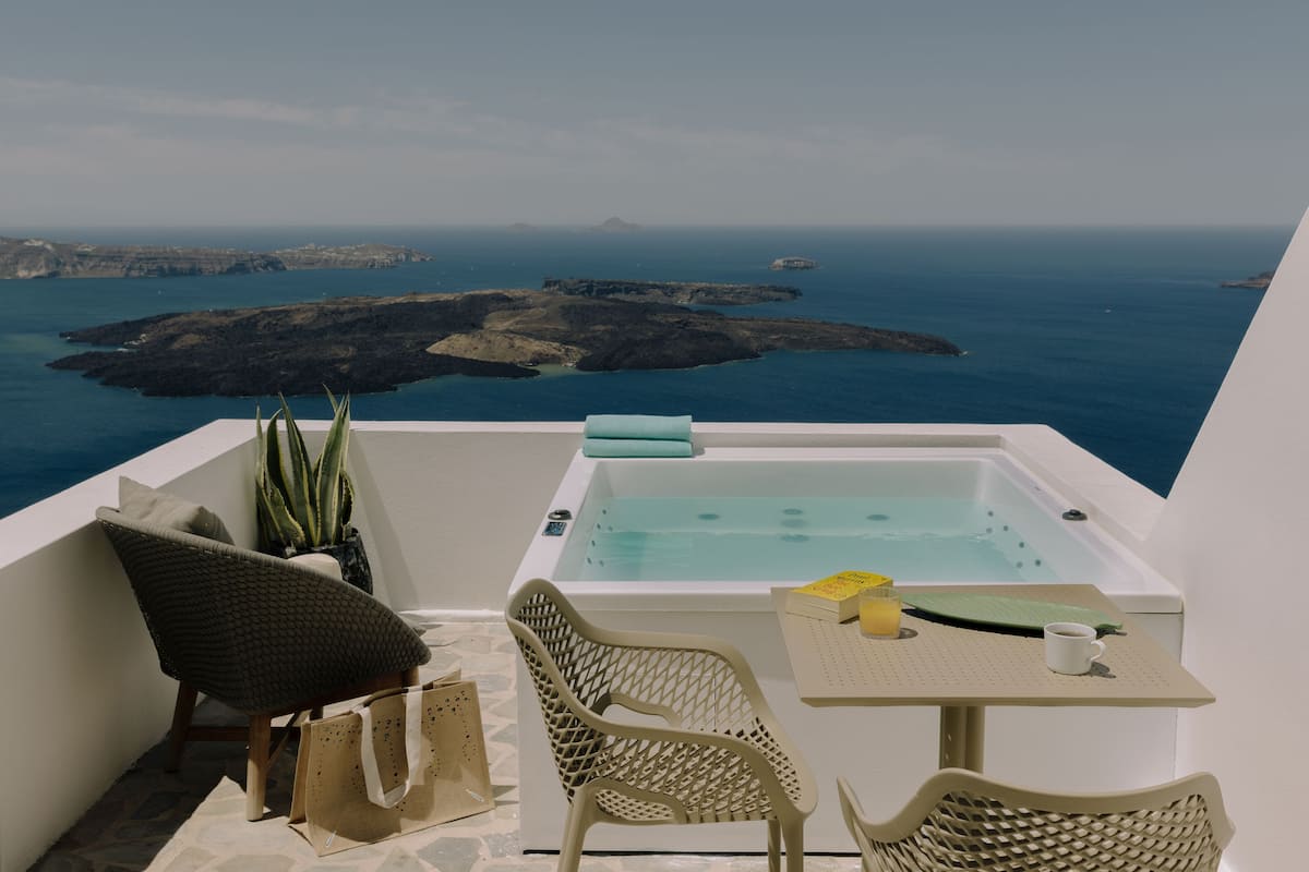 A balcony with a hot tub, wicker chairs, a table with a cup, and a view of the sea and islands.