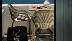Un balcon avec deux fauteuils en osier, un vase blanc, un livre et un sac noir.