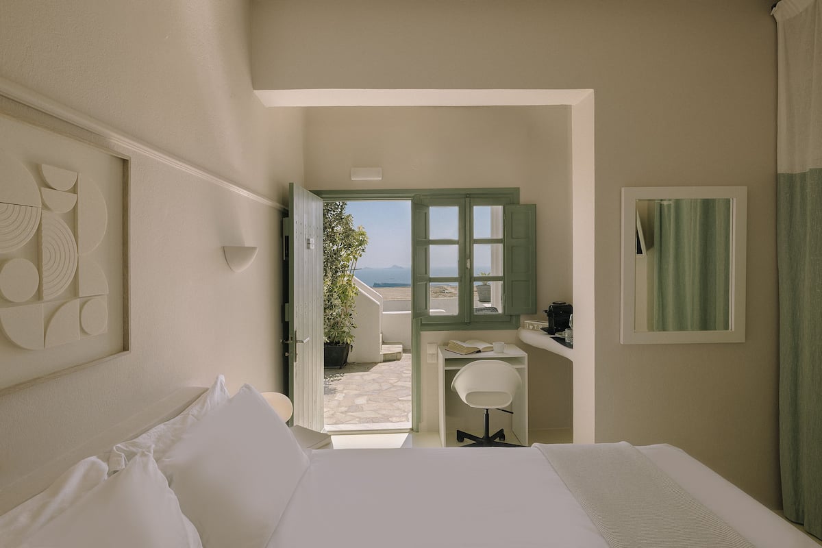 A bedroom with a bed, a desk, and a view of the outdoors.