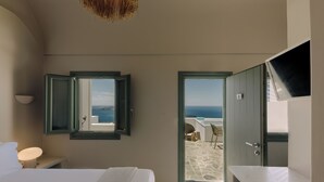 Une chambre à coucher avec un lit, une table de chevet, une lampe et une vue sur la mer par une porte ouverte.