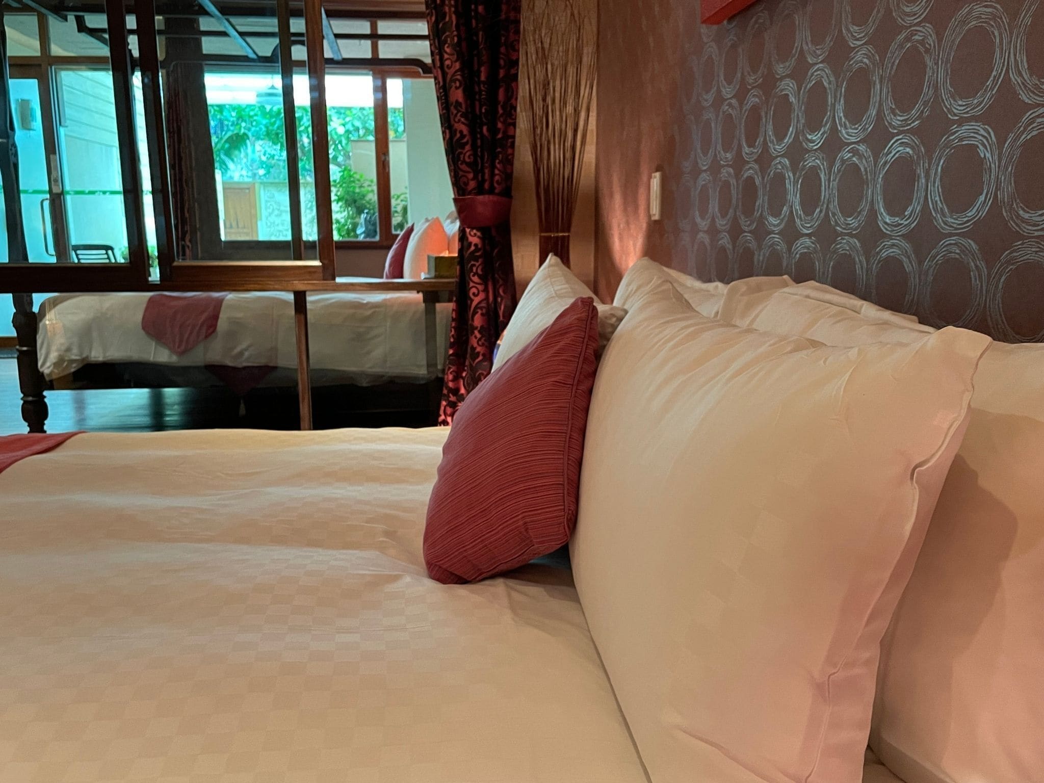 A hotel room with a bed, a window, and a view of greenery outside.