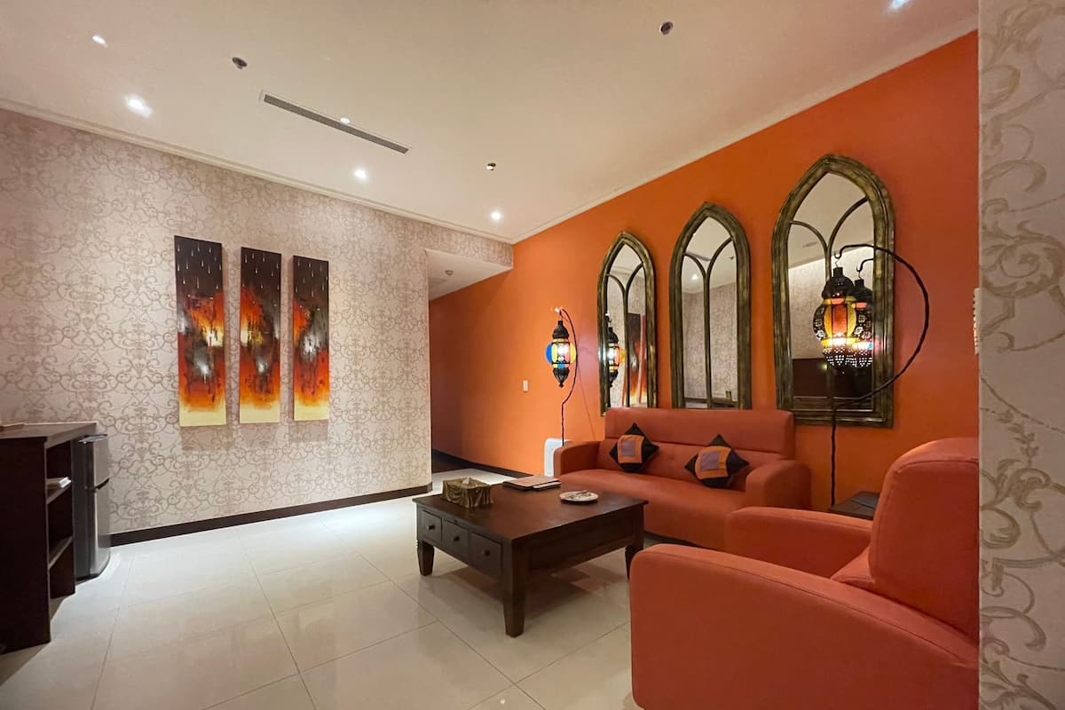 A modern living room with a sofa, a coffee table, and a TV. There are three wall-mounted paintings and a decorative mirror.