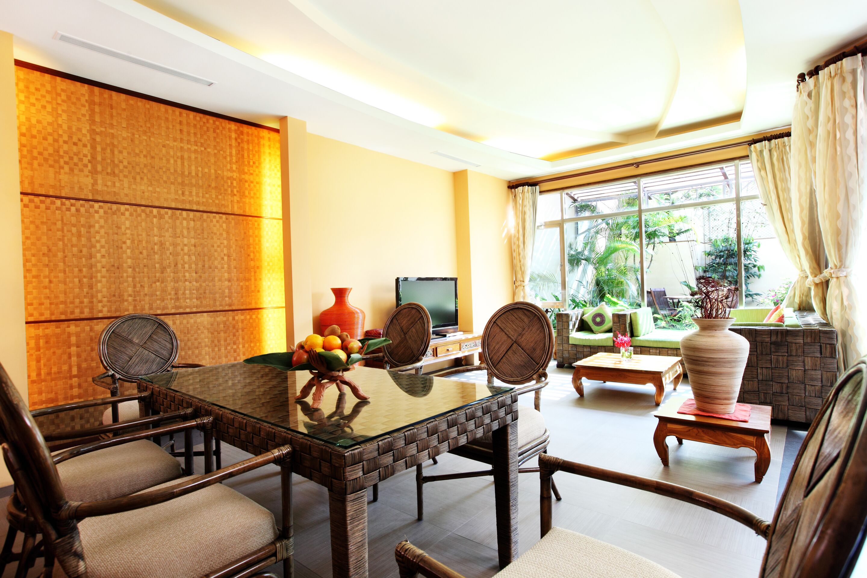 A dining area with a glass-top table, wicker chairs, and a television.