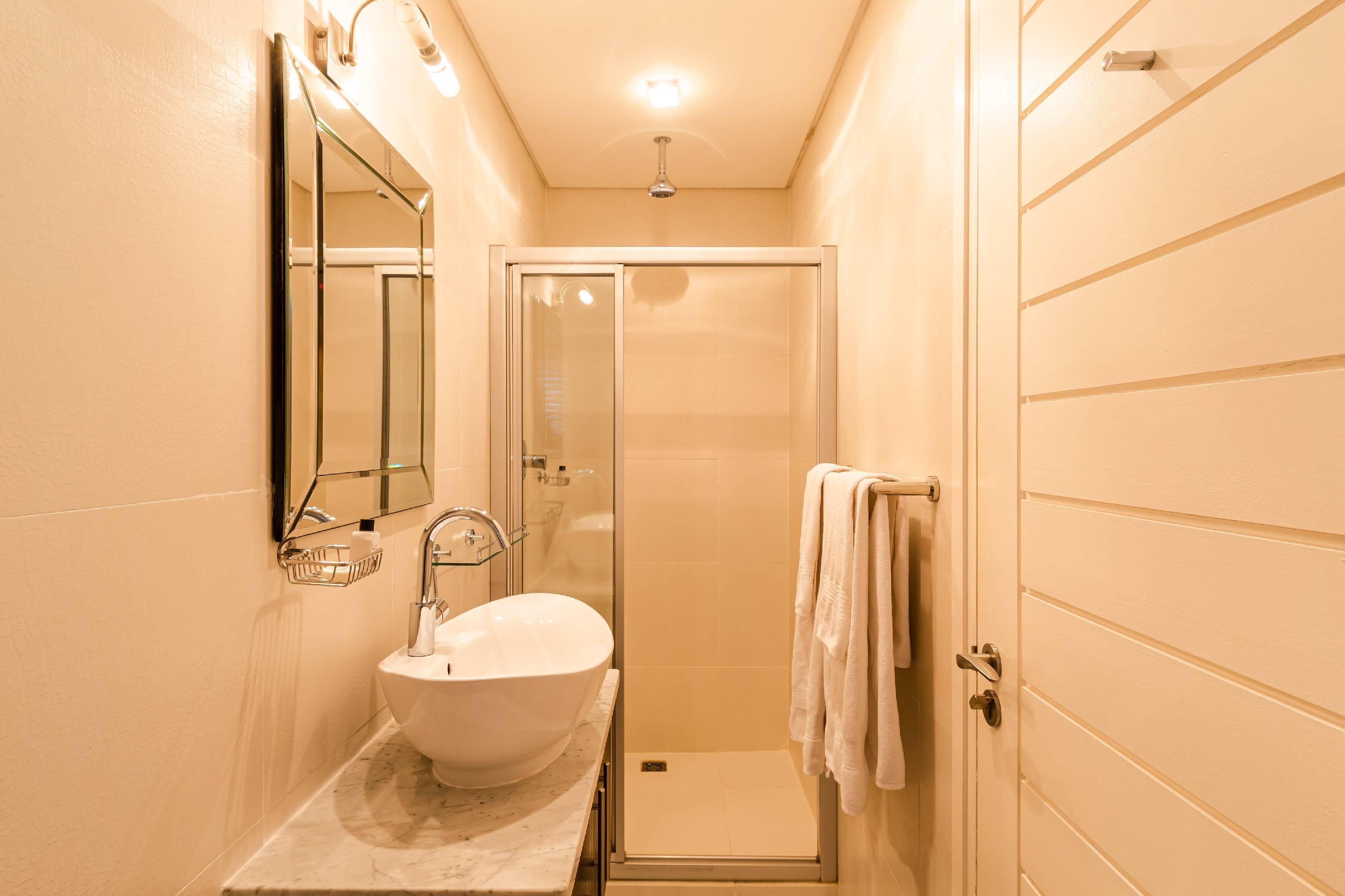 A modern bathroom with a large white sink, a glass shower enclosure, and a towel rack.