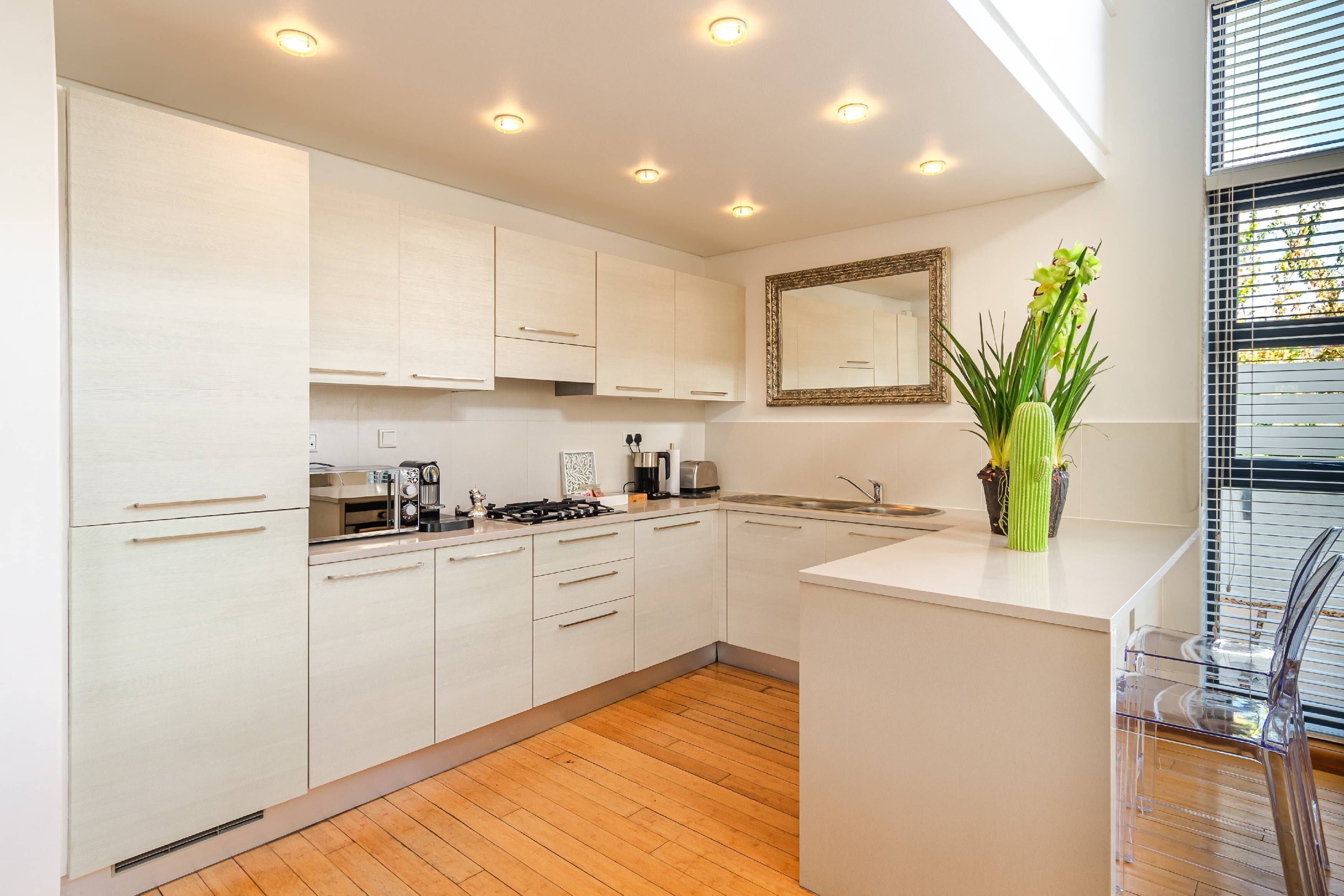 A modern kitchen with white cabinets, a central island, and a large window with blinds.