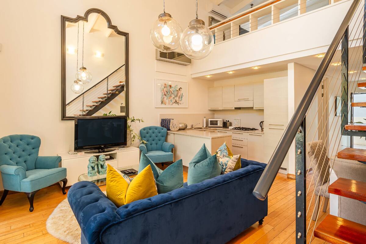 Ein modernes Wohnzimmer mit einem blauen Sofa, zwei Sesseln, einem Fernseher und einer Treppe, die in einen oberen Bereich führt.