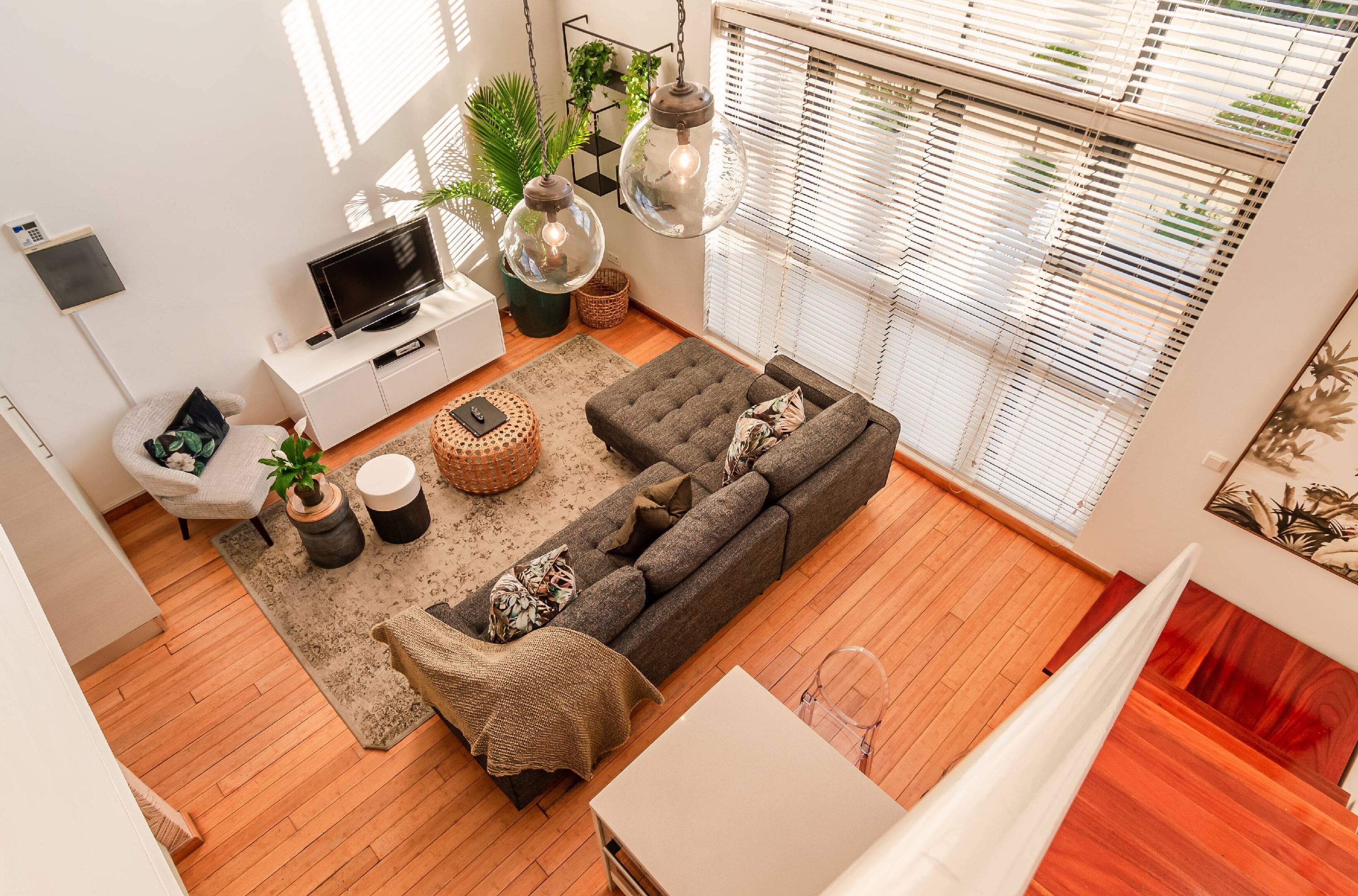 A modern living room with a grey sofa, a flat-screen TV, and hanging pendant lights.