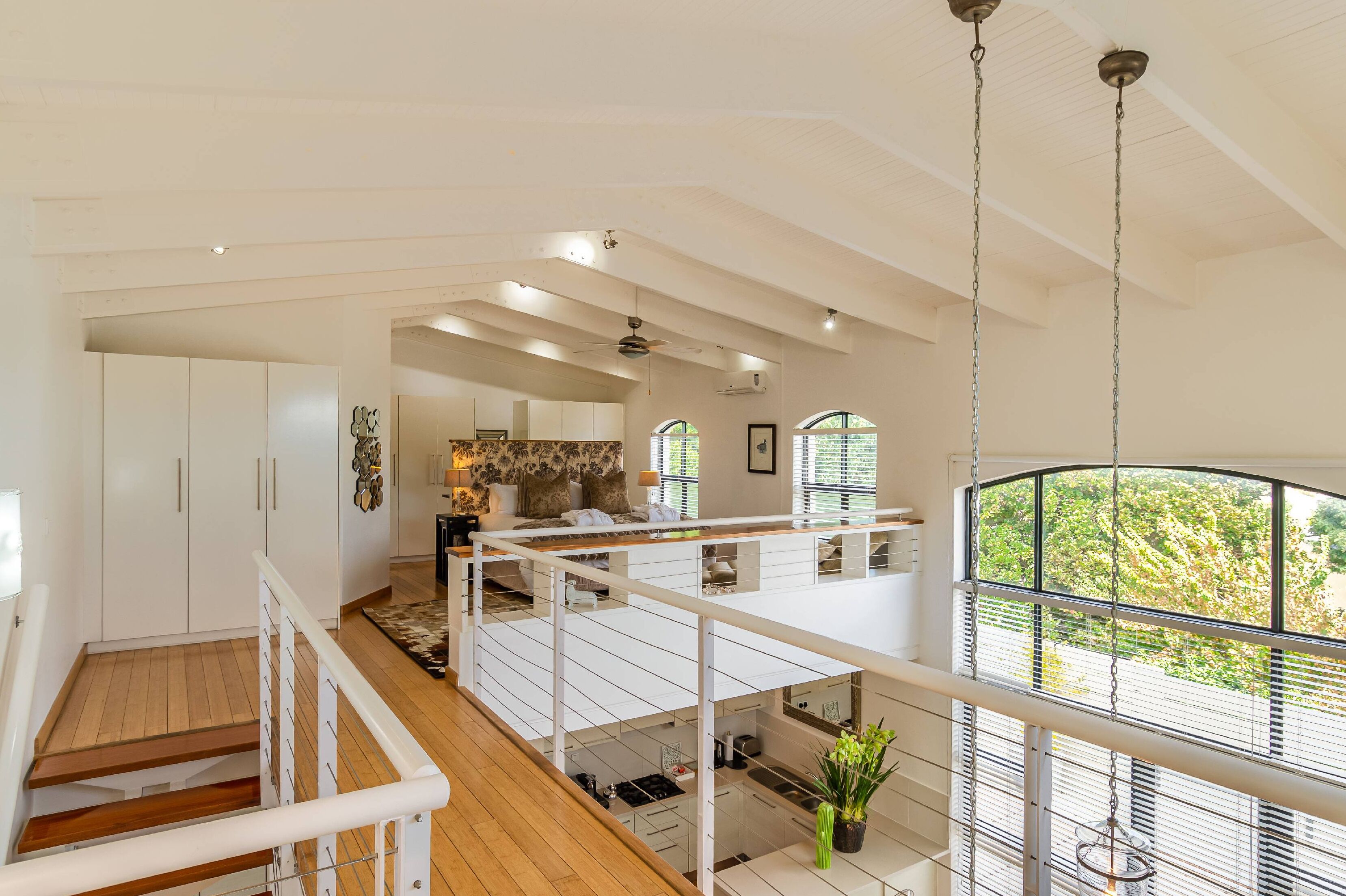 A spacious loft-style apartment with a high ceiling, open-plan living area, kitchen, and a balcony with a view of the outdoors.
