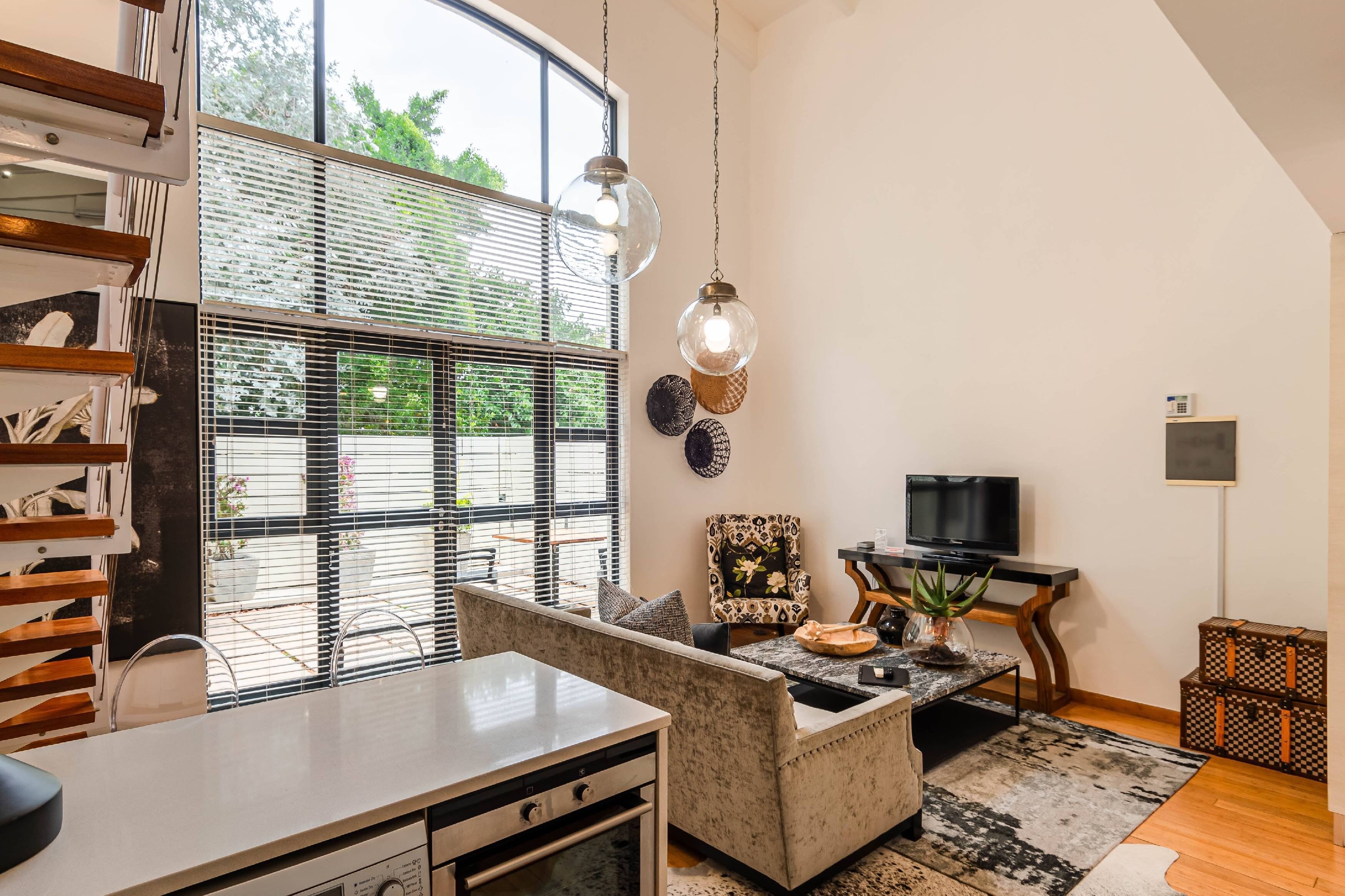 A modern living room with a large window, a sofa, a coffee table, a TV, and a bookshelf.
