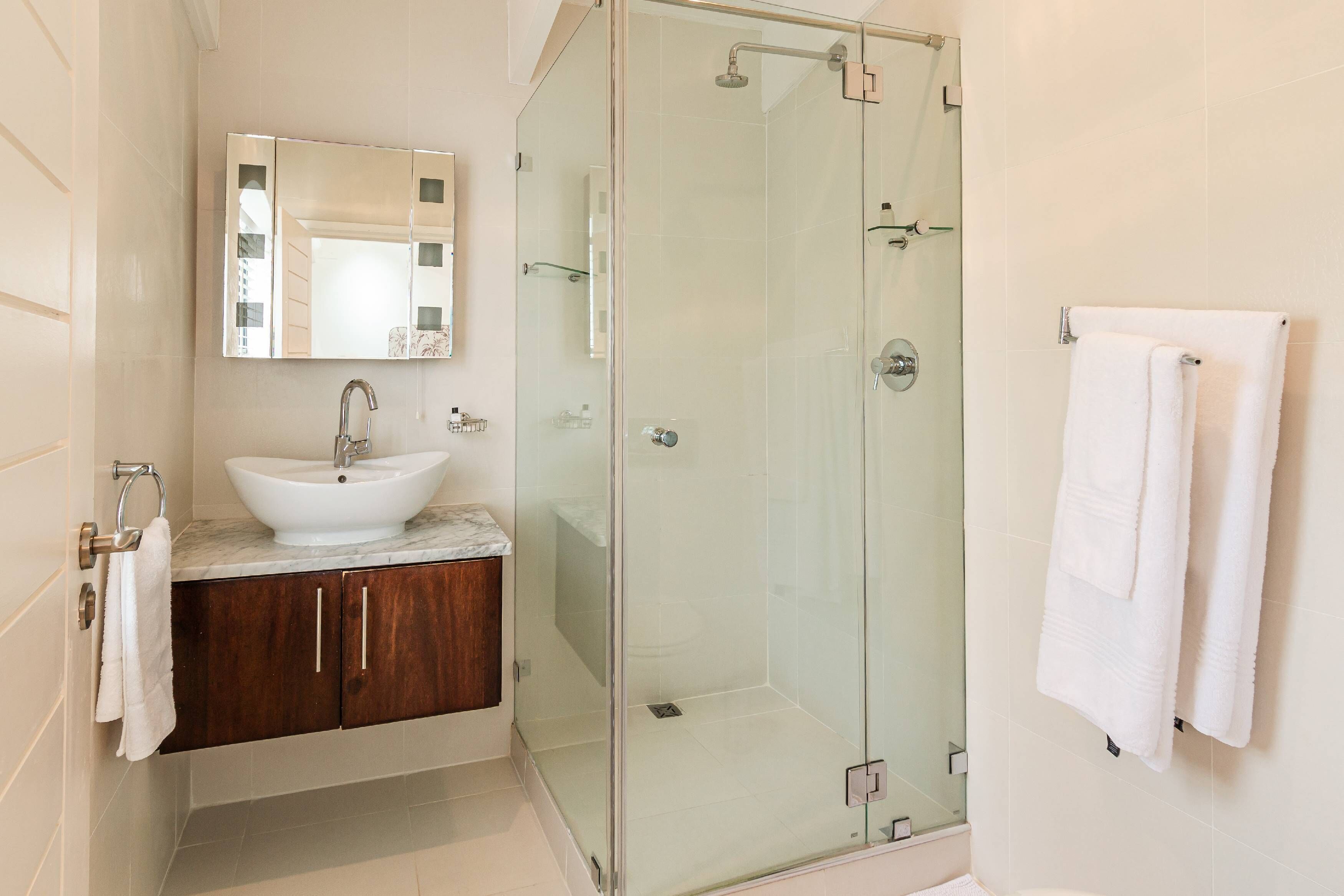 Een moderne badkamer met een douchecabine van glas, een witte wastafel en houten kastjes.
