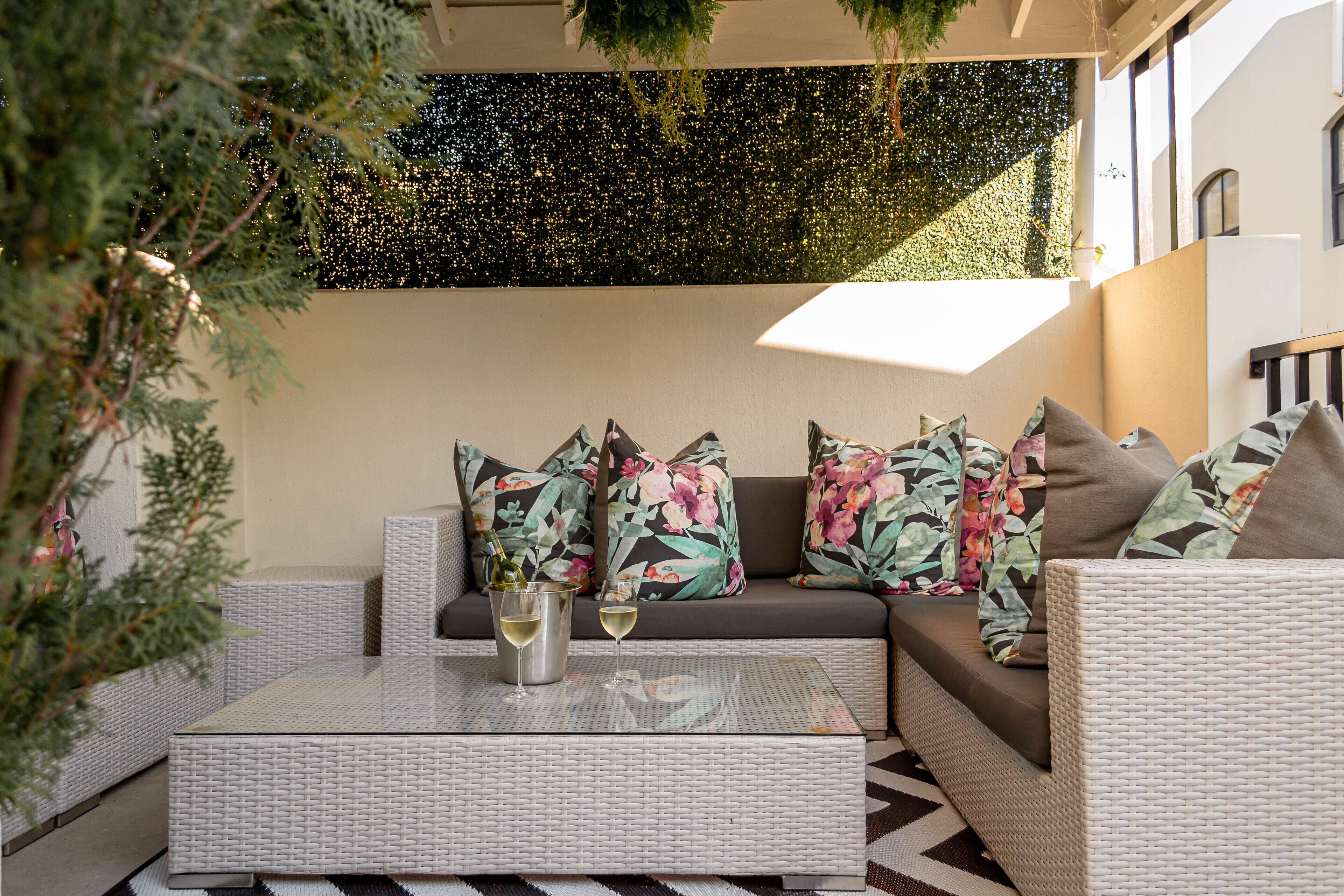 A modern outdoor seating area with a sofa and a coffee table, a decorative wall, and a potted plant.