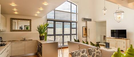 A modern kitchen with a central island, a dining area with patterned cushions, and a large window with blinds.