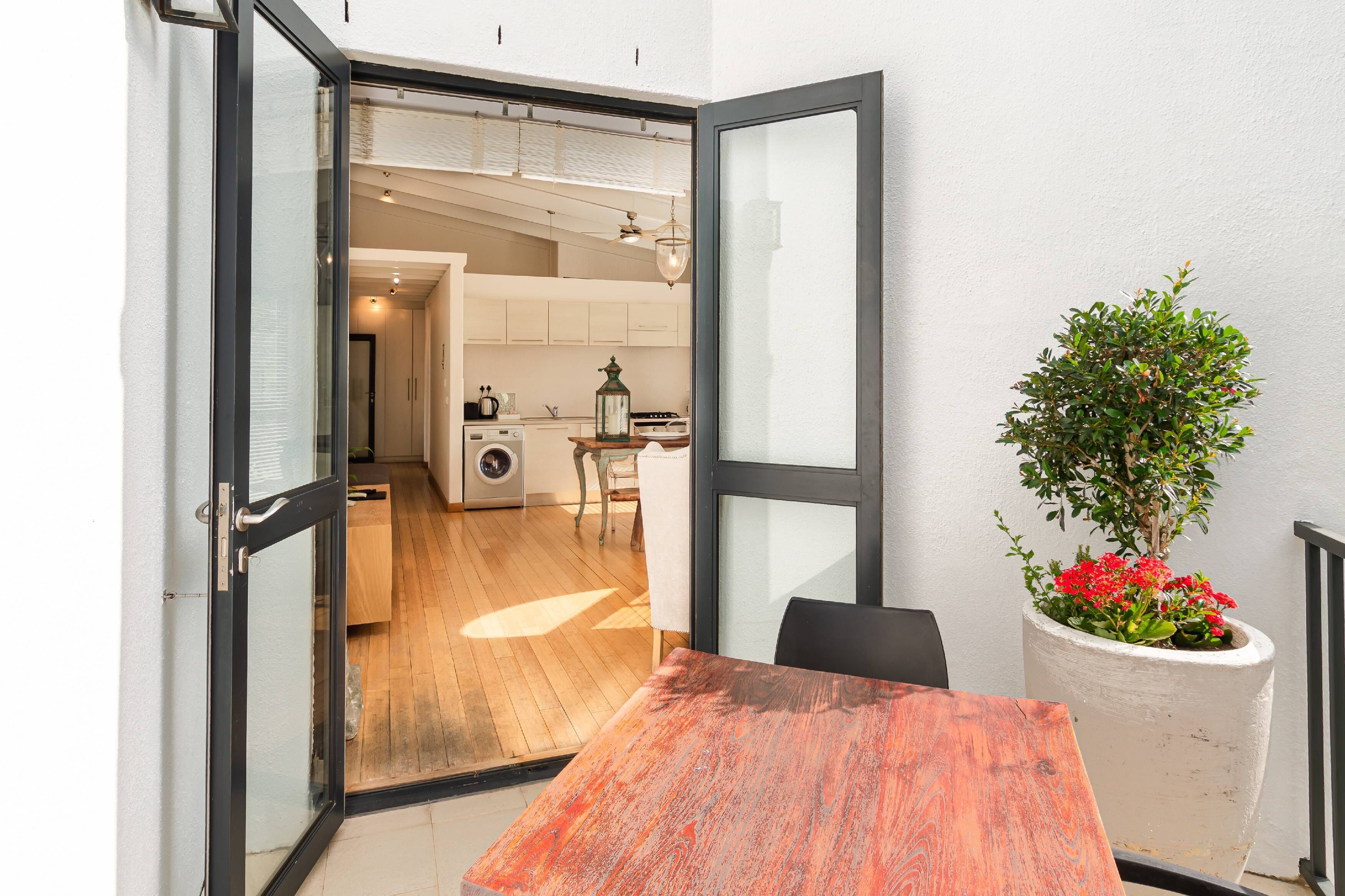 An open door leading to a kitchen with wooden flooring, a dining table, and a potted plant.