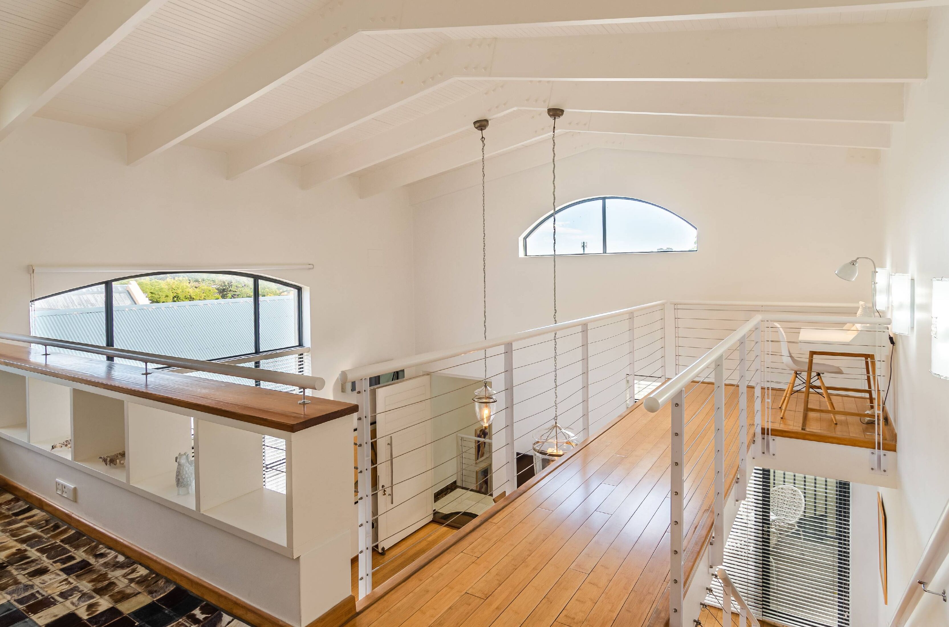 Un loft spacieux avec de hauts plafonds, un plancher en bois, une mezzanine avec une balustrade et une grande fenêtre en arc de cercle qui laisse entrer la lumière naturelle.