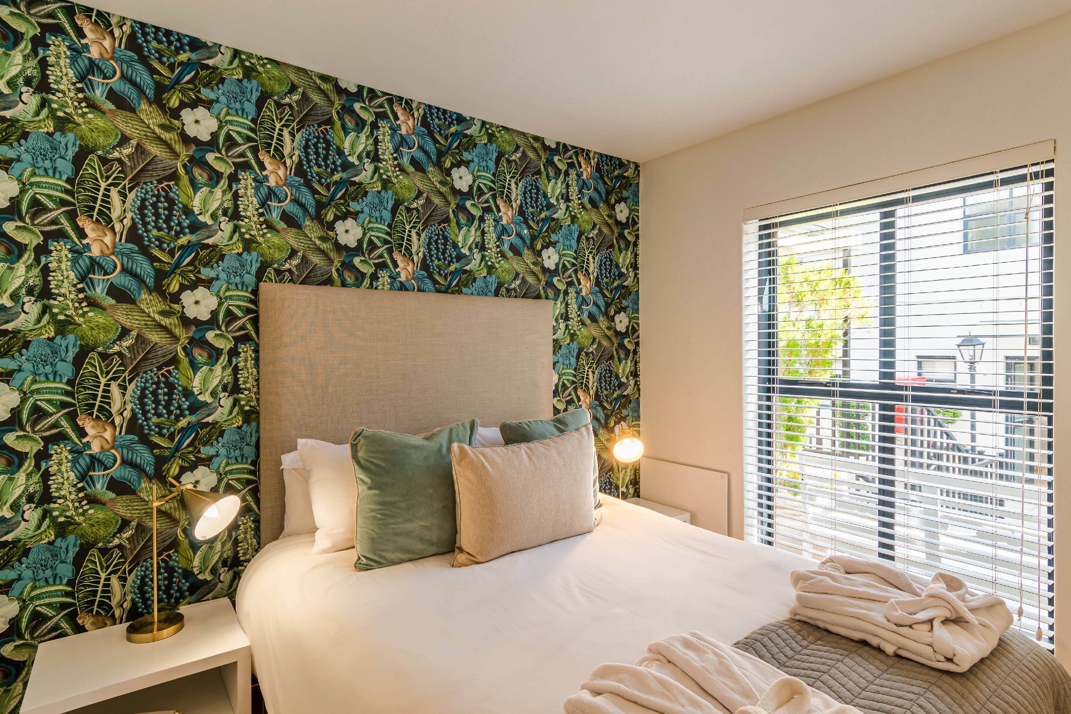 A hotel room with a bed, nightstands, a lamp, and a window with blinds.