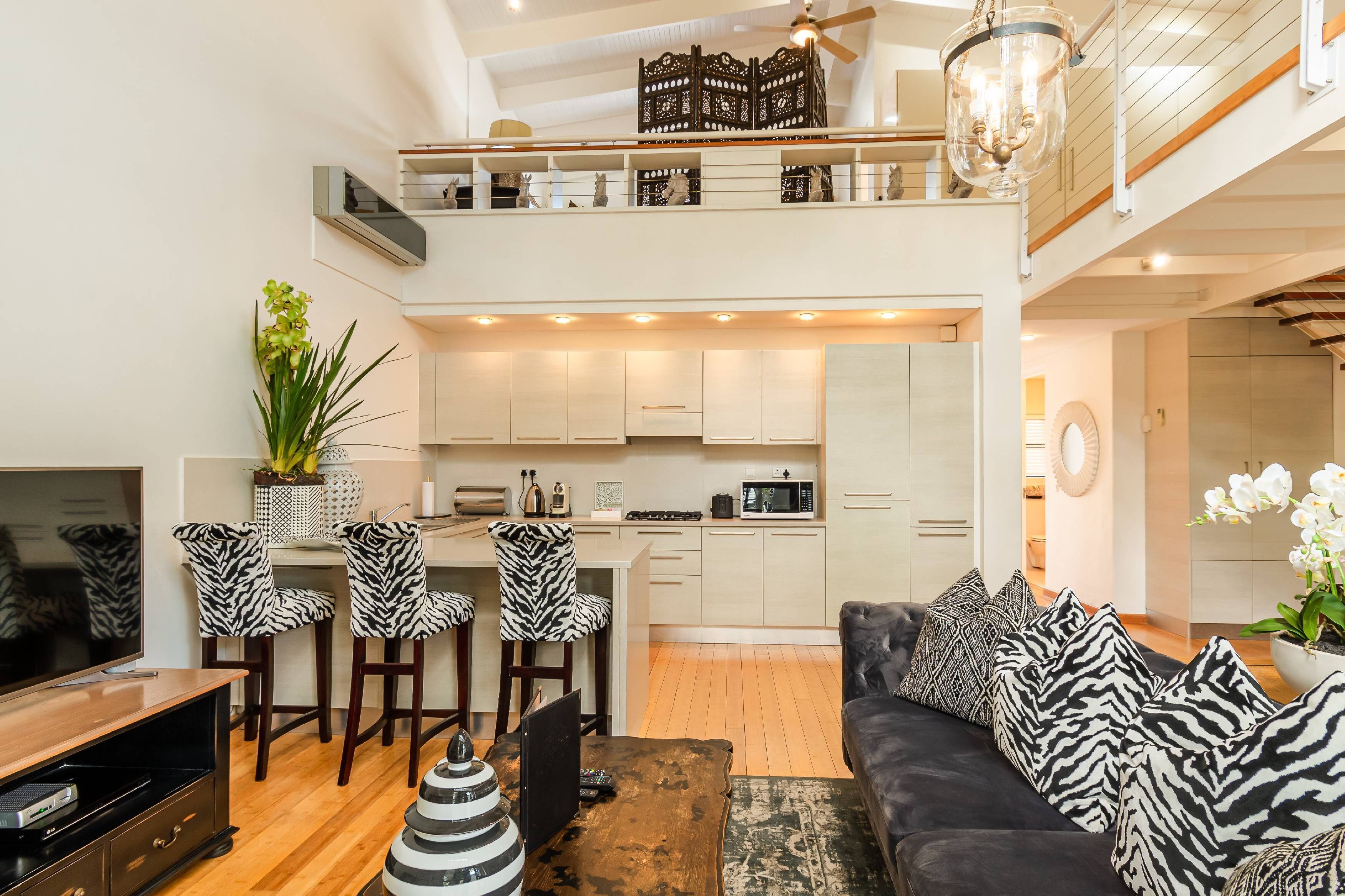 A modern living room with a black sofa, zebra-striped chairs, a wooden coffee table, and a TV stand.