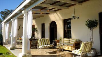 Relax in a serene outdoor seating area with a wooden bench, metal-framed chair, and sofa, surrounded by lush greenery and an arched doorway.