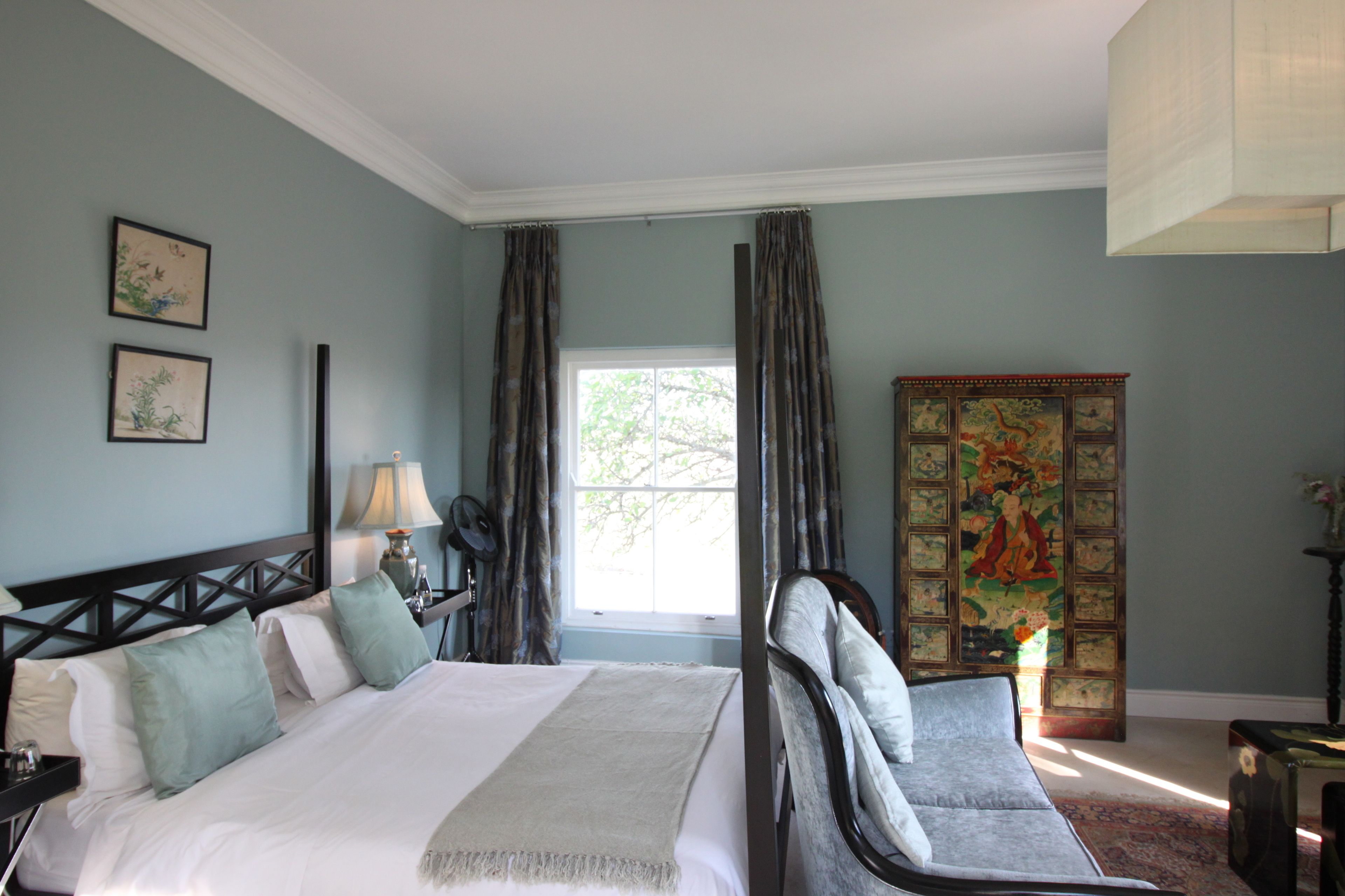 A bedroom with a large bed, a chair, a nightstand, a lamp, and a window with curtains.