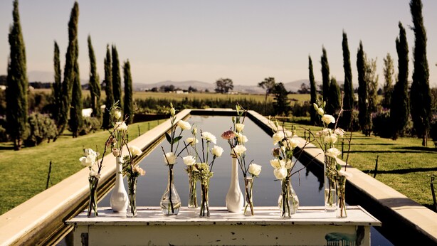 A row of vases with flowers on a ledge by a water feature. - Hawksmoor House (Cape Town)