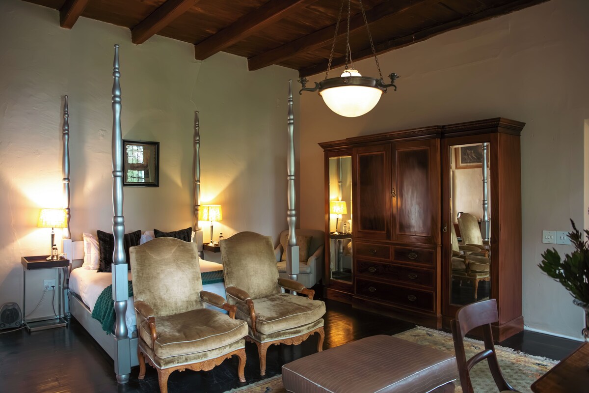 A hotel room with a bed, two armchairs, a wooden cabinet, and a hanging light fixture.