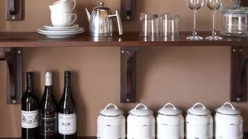 Una cocina con estantes de madera, botellas de vino y recipientes de almacenamiento blancos.