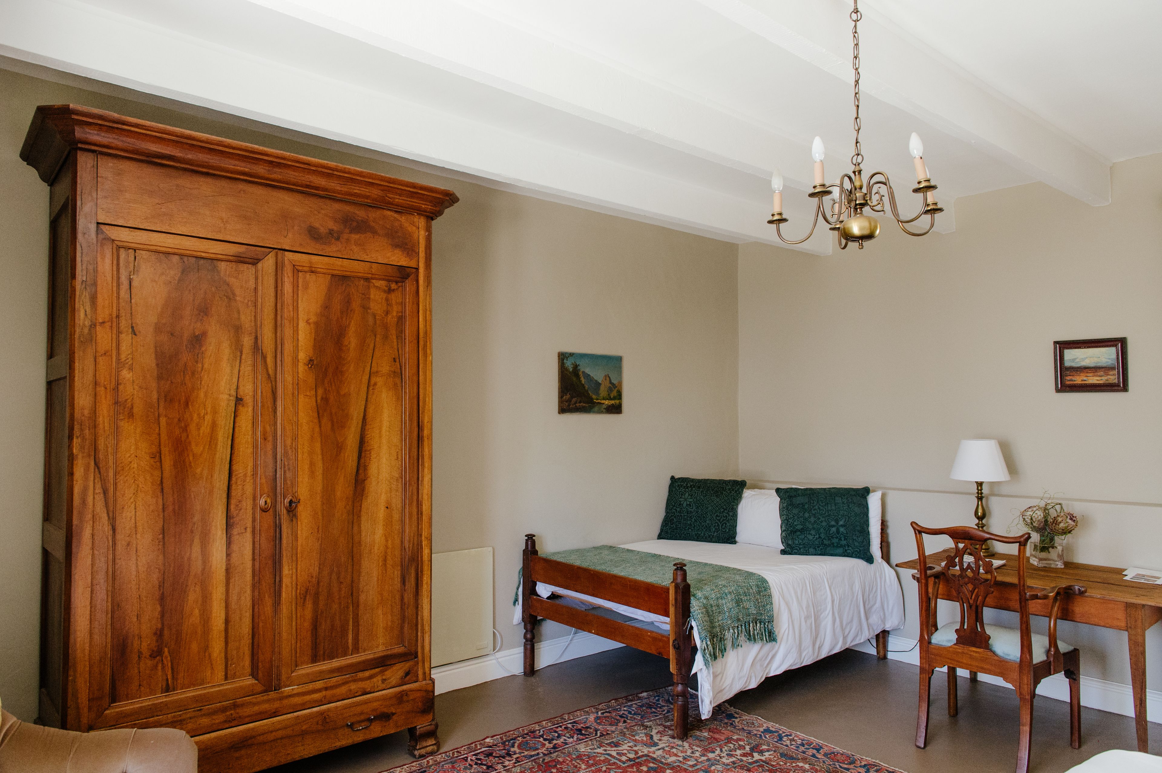 Un dormitorio con un armario de madera, una cama con almohada verde, una araña y un escritorio con lámpara.