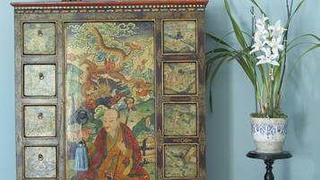 Un mueble tradicional con intrincados detalles decorativos, una mesita con una planta en maceta y una lámpara ornamental.
