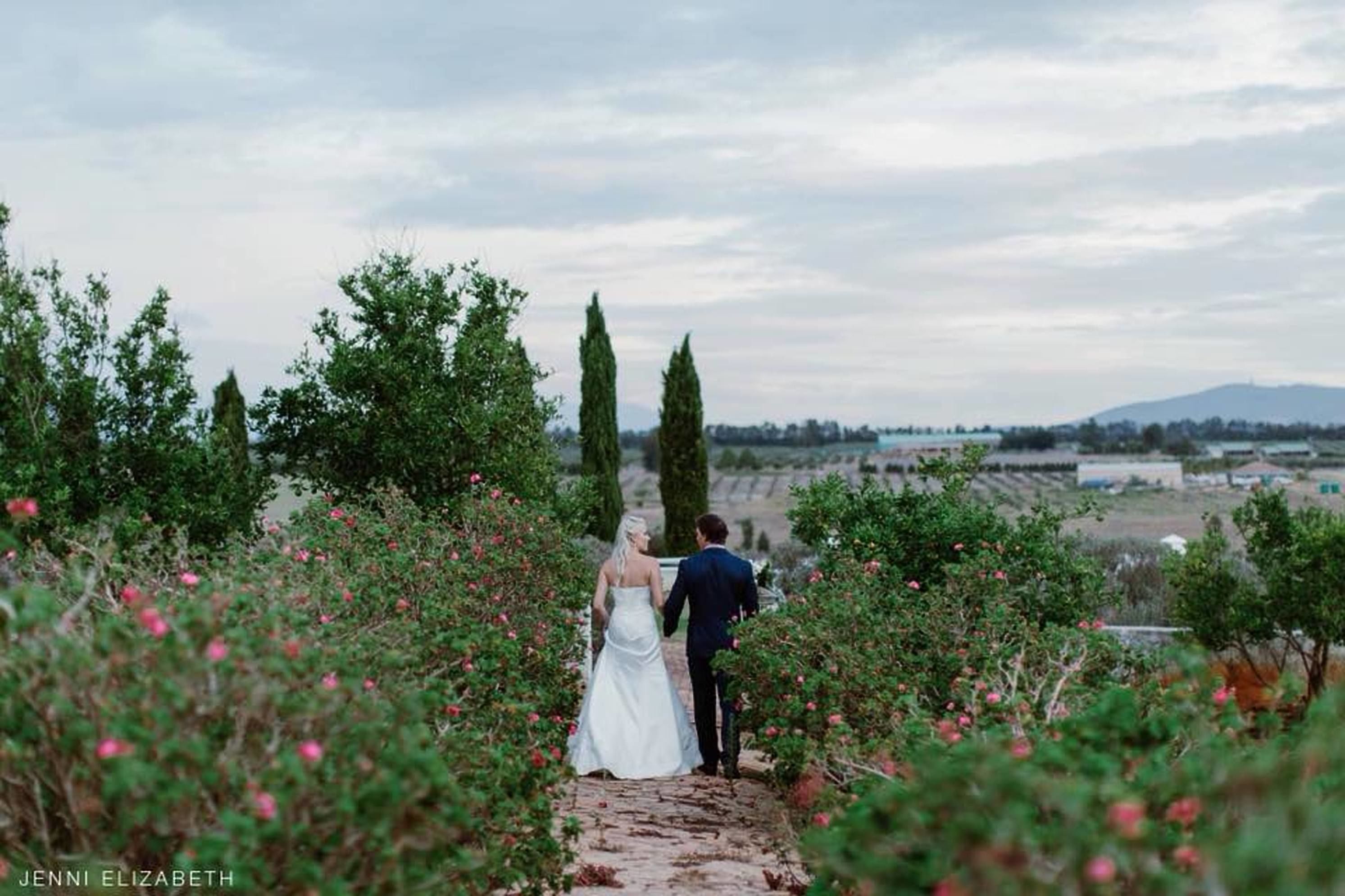 Una pareja caminando por un sendero rodeado de vegetación y flores.